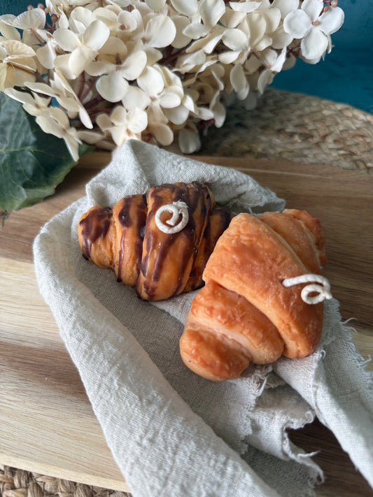 Detailreiche Croissant-Duftkerze in realistischer Gebäckoptik mit goldbrauner Oberfläche und geschichteten Butterteig-Details. Die handgegossene Kerze erinnert an ein frisch gebackenes französisches Croissant aus einer Patisserie und verströmt einen warmen, süßen Duft. Stilvoll dekoriert auf hellem Untergrund im minimalistischen Café- und Interior-Stil.