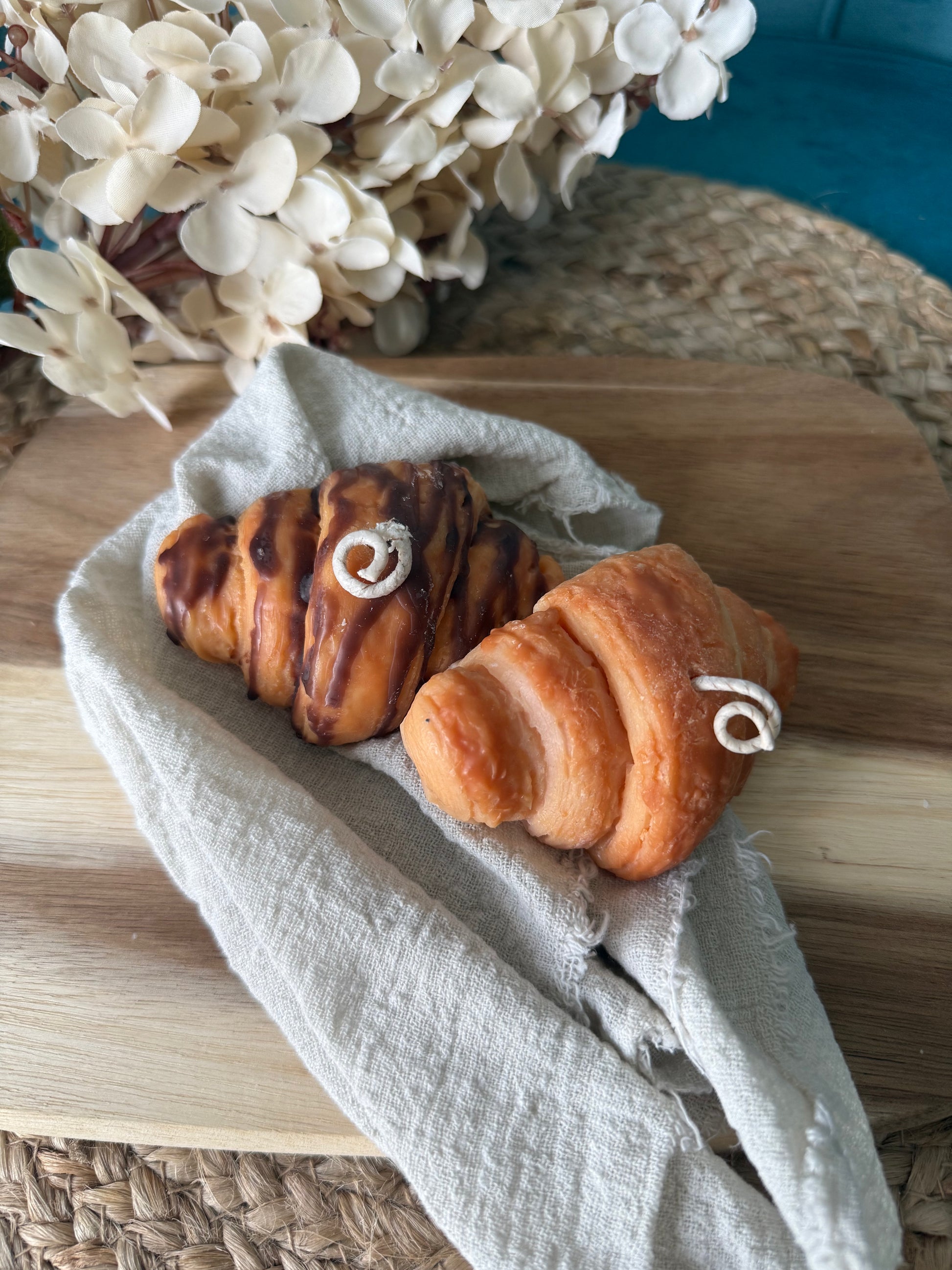 Detailreiche Croissant-Duftkerze in realistischer Gebäckoptik mit goldbrauner Oberfläche und geschichteten Butterteig-Details. Die handgegossene Kerze erinnert an ein frisch gebackenes französisches Croissant aus einer Patisserie und verströmt einen warmen, süßen Duft. Stilvoll dekoriert auf hellem Untergrund im minimalistischen Café- und Interior-Stil.