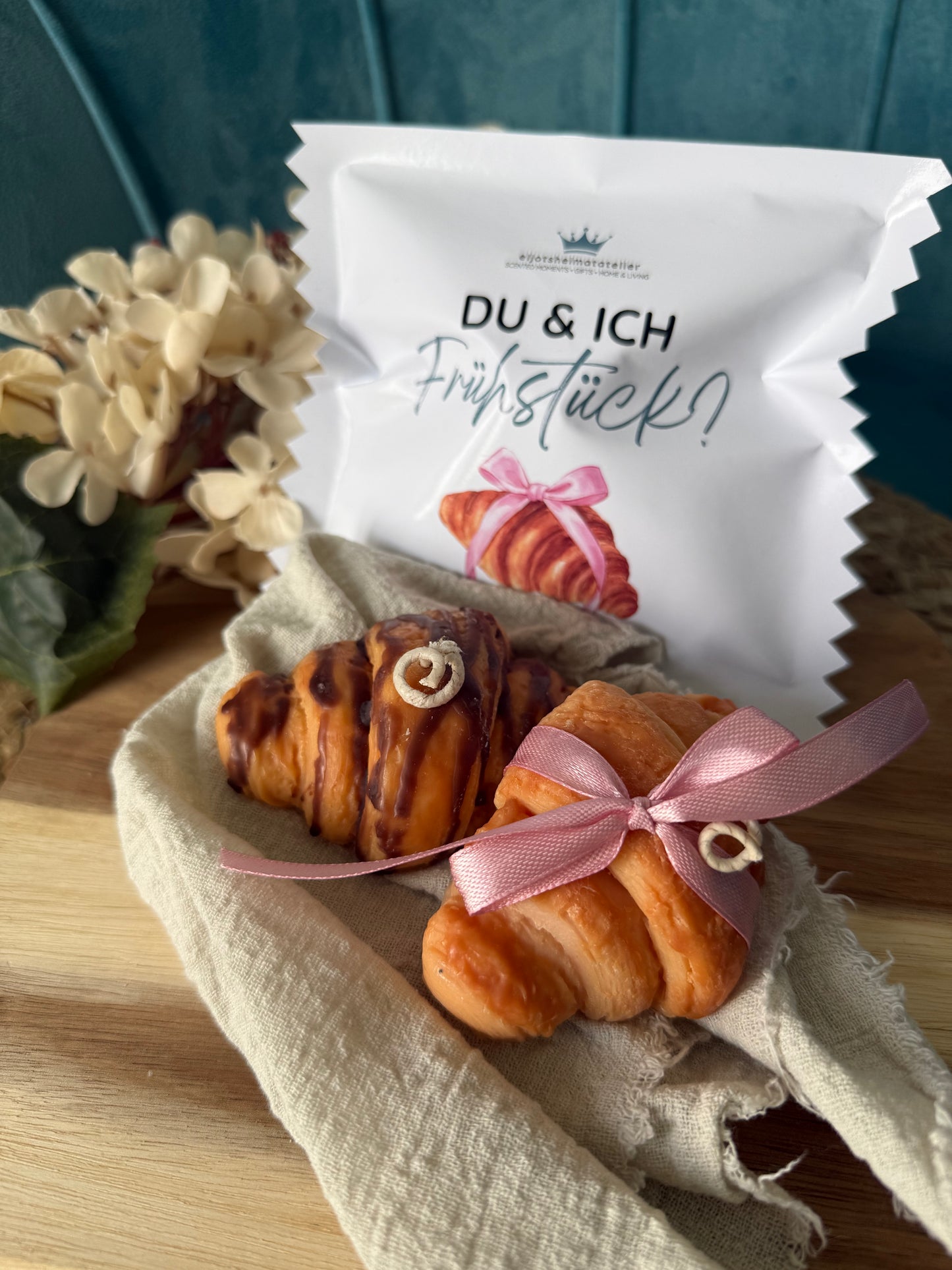 Detailreiche Croissant-Duftkerze in realistischer Gebäckoptik mit goldbrauner Oberfläche und geschichteten Butterteig-Details. Die handgegossene Kerze erinnert an ein frisch gebackenes französisches Croissant aus einer Patisserie und verströmt einen warmen, süßen Duft. Stilvoll dekoriert auf hellem Untergrund im minimalistischen Café- und Interior-Stil.